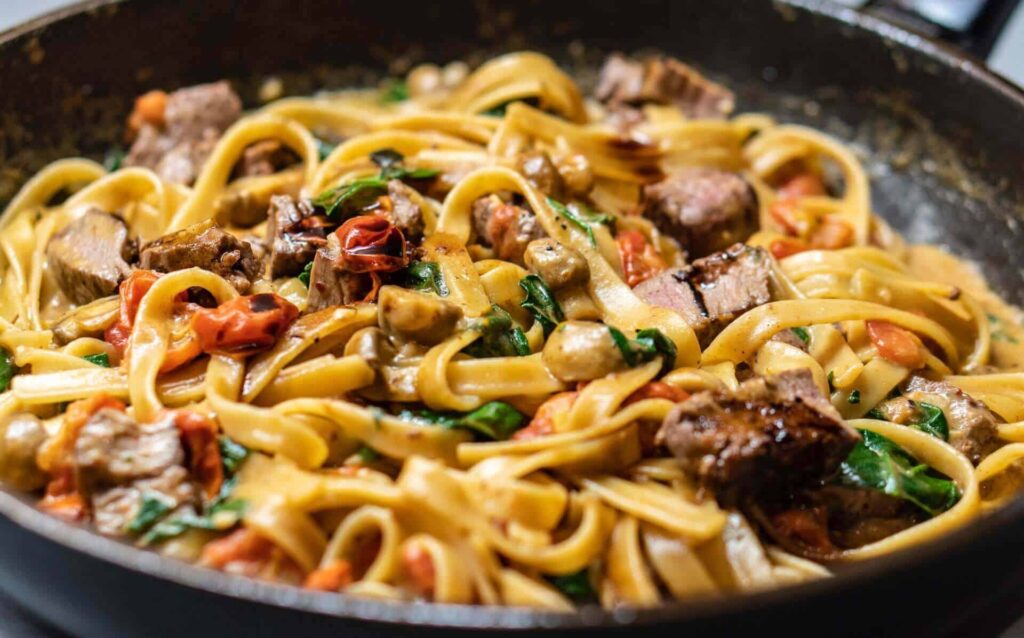 Linguine with pancetta, mushrooms, tomatoes and herbs sautéed in a skillet.
