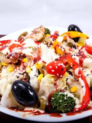 Colorful pasta salad on a white plate with olives, broccoli, tomatoes, corn, and a creamy dressing.